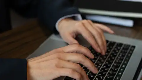 Hände auf der Tastatur eines Laptops im Licht eines Schreibtisches